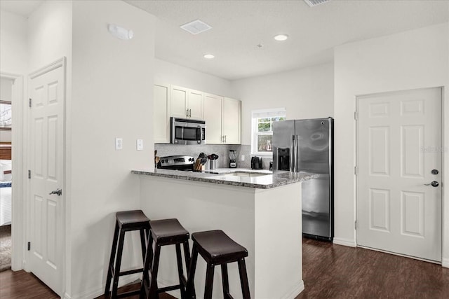 kitchen with a kitchen bar, dark stone counters, white cabinets, dark hardwood / wood-style flooring, and stainless steel appliances