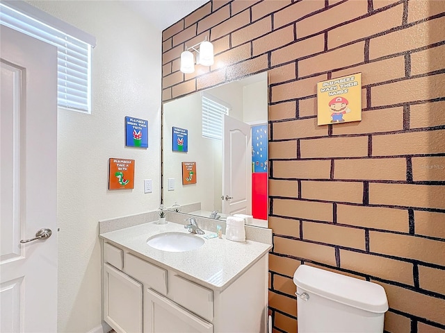 bathroom featuring vanity, toilet, and brick wall