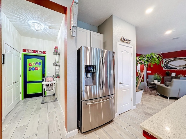 kitchen featuring stainless steel fridge with ice dispenser, a textured ceiling, white cabinetry, and light hardwood / wood-style flooring