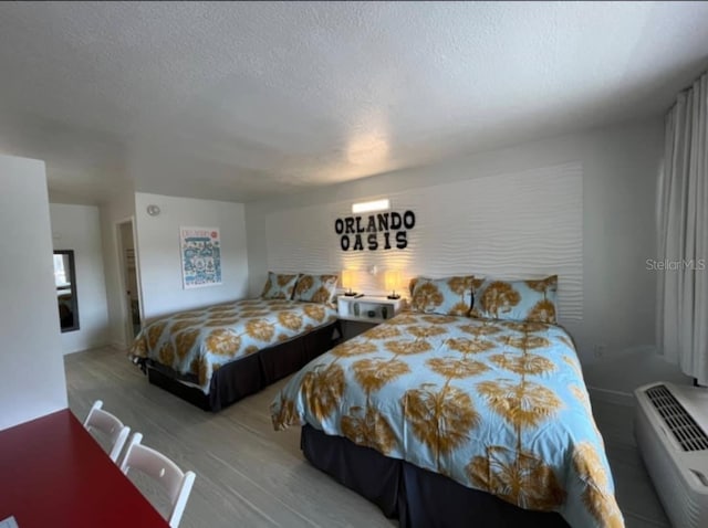 bedroom with a wall mounted air conditioner, light wood-type flooring, and a textured ceiling