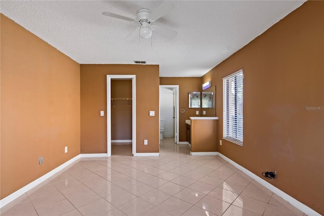 unfurnished bedroom with a walk in closet, ceiling fan, light tile patterned floors, a textured ceiling, and a closet