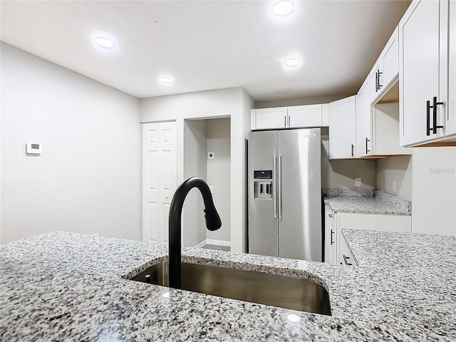 kitchen with stainless steel fridge with ice dispenser, sink, white cabinets, and light stone countertops