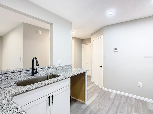 kitchen with light hardwood / wood-style floors, light stone counters, white cabinetry, and sink