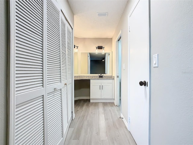 corridor featuring light hardwood / wood-style flooring, a textured ceiling, and sink