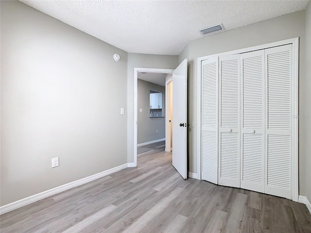 unfurnished bedroom with a closet, a textured ceiling, and light hardwood / wood-style flooring