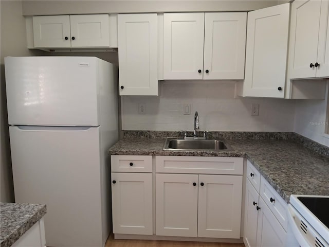kitchen featuring stove, a sink, freestanding refrigerator, and white cabinets