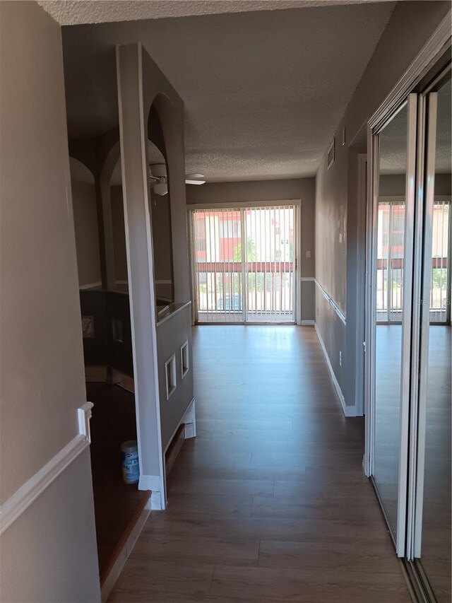 hall featuring a textured ceiling, wood finished floors, visible vents, and baseboards