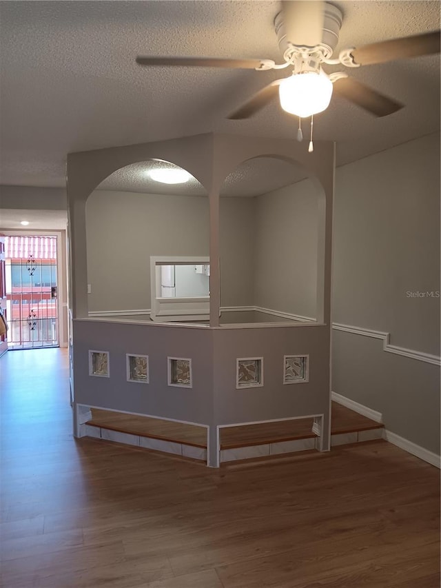spare room featuring a textured ceiling, wood finished floors, a ceiling fan, and baseboards