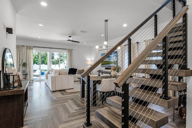 staircase with ceiling fan with notable chandelier and parquet flooring