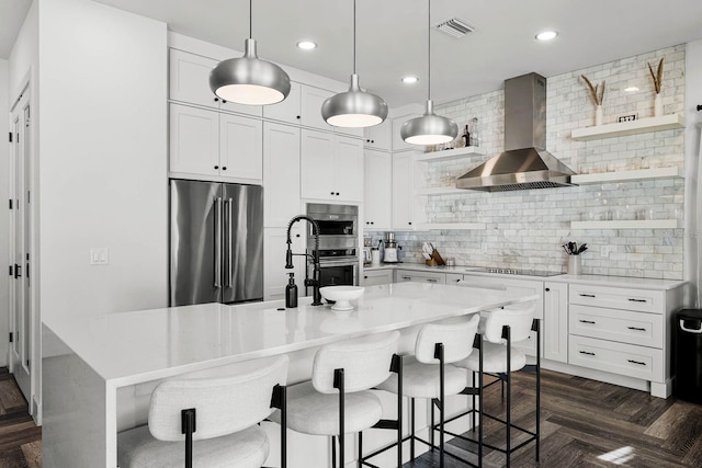 kitchen featuring dark parquet flooring, wall chimney range hood, backsplash, white cabinets, and appliances with stainless steel finishes