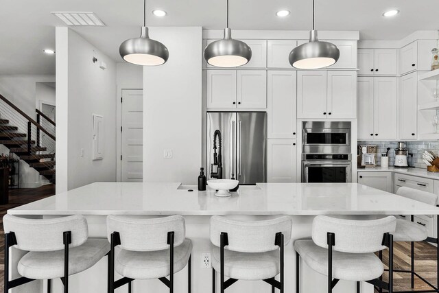 kitchen featuring backsplash, stainless steel appliances, pendant lighting, a center island, and white cabinetry