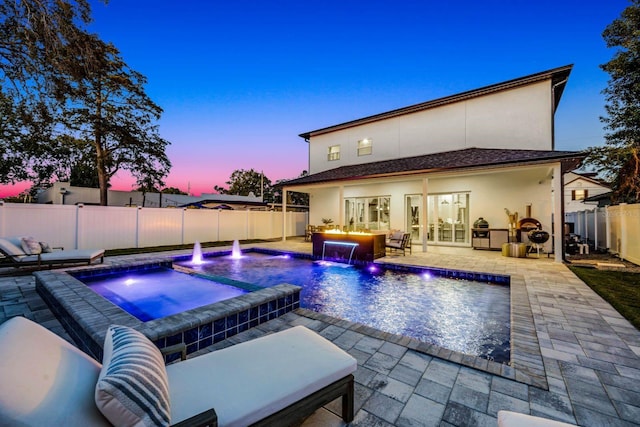 pool at dusk featuring an in ground hot tub, pool water feature, and a patio