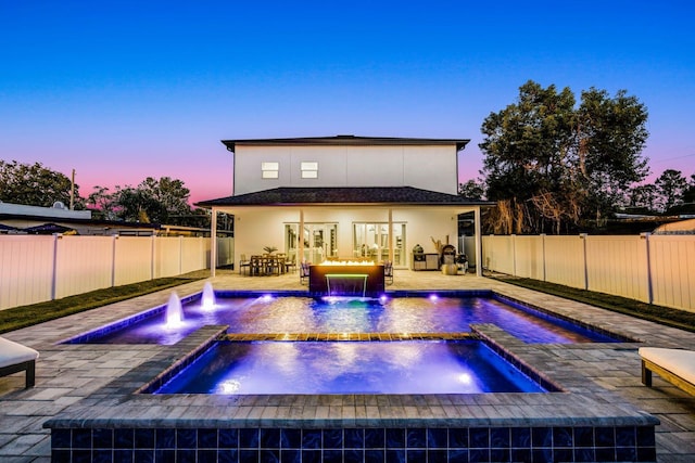 pool at dusk featuring pool water feature, an in ground hot tub, and a patio