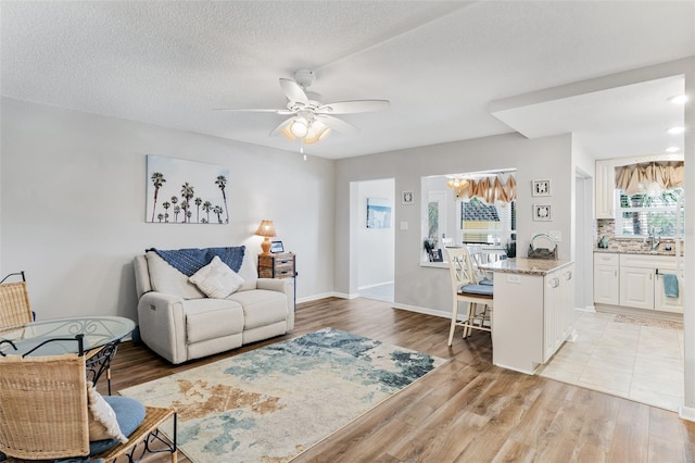 living room featuring a textured ceiling, light wood-type flooring, ceiling fan, and sink