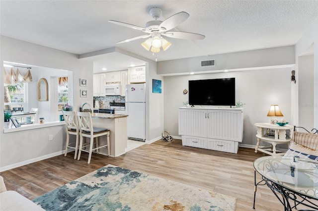 living room with a textured ceiling, light hardwood / wood-style flooring, ceiling fan, and sink