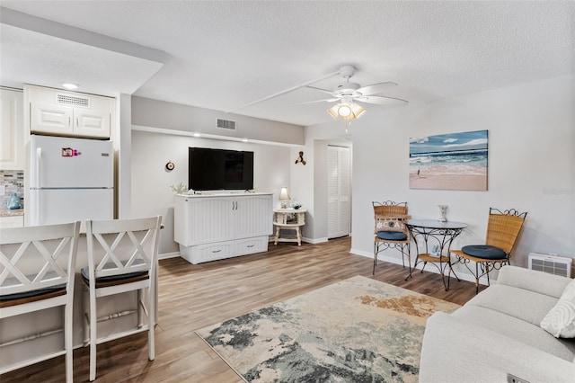 living room featuring a textured ceiling, light wood-type flooring, and ceiling fan