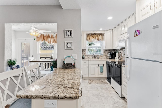 kitchen with white appliances, white cabinetry, ceiling fan, and sink