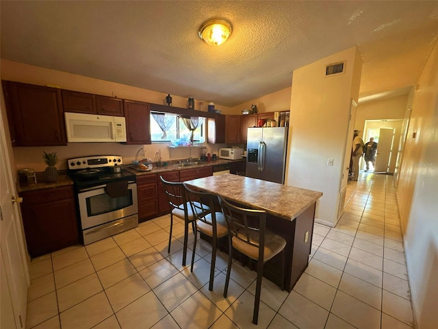 kitchen with vaulted ceiling, light tile patterned floors, a textured ceiling, a kitchen island, and stainless steel appliances