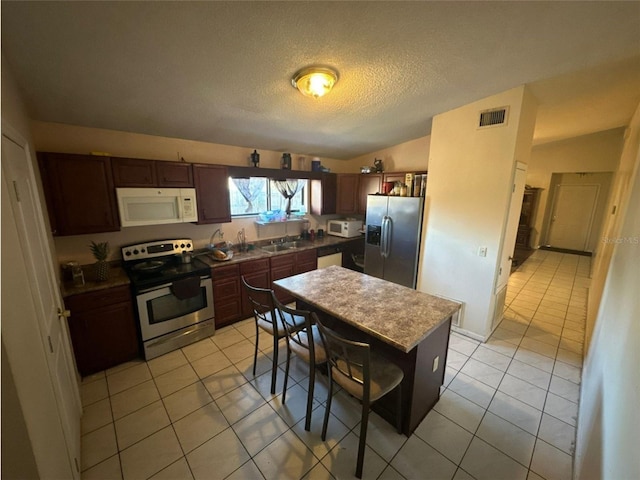 kitchen featuring visible vents, light tile patterned flooring, a breakfast bar, a textured ceiling, and appliances with stainless steel finishes