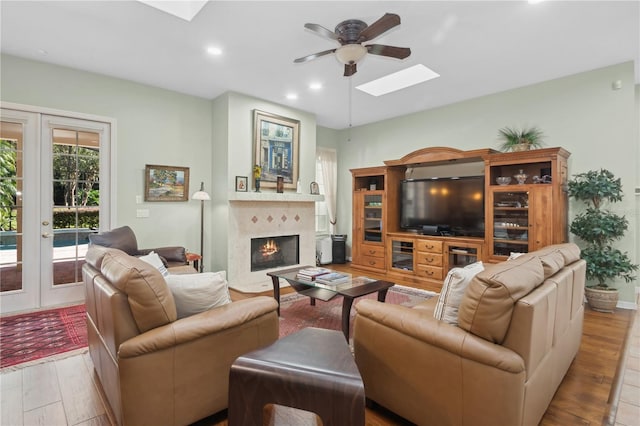 living room with french doors, a skylight, light wood-type flooring, ceiling fan, and a fireplace