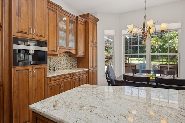 kitchen featuring decorative backsplash, hanging light fixtures, wall oven, light stone countertops, and an inviting chandelier