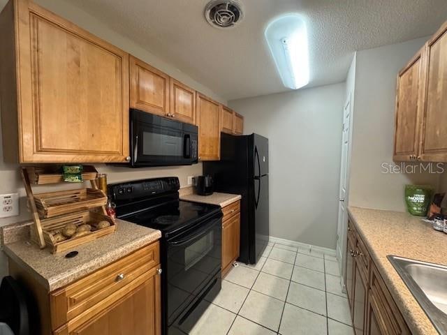 kitchen with black appliances, light tile patterned floors, sink, and a textured ceiling