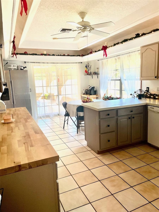 kitchen with stainless steel fridge with ice dispenser, kitchen peninsula, white dishwasher, a textured ceiling, and a tray ceiling