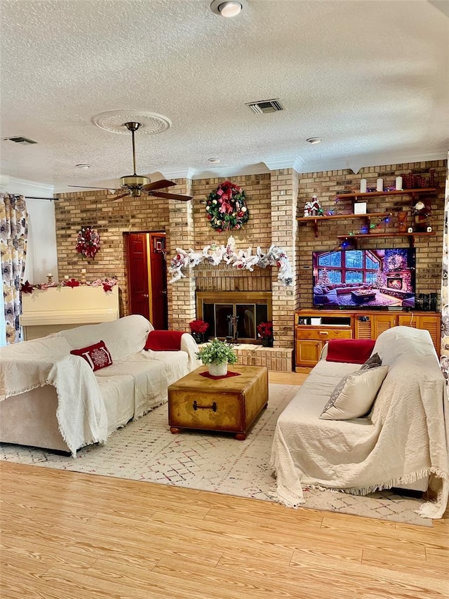 living room with a fireplace, a textured ceiling, light hardwood / wood-style floors, and brick wall