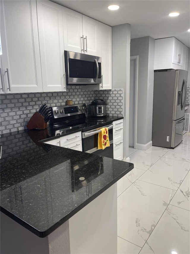 kitchen with white cabinets, kitchen peninsula, appliances with stainless steel finishes, and tasteful backsplash