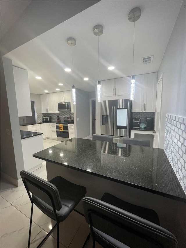 kitchen with a kitchen bar, kitchen peninsula, backsplash, stainless steel appliances, and white cabinetry