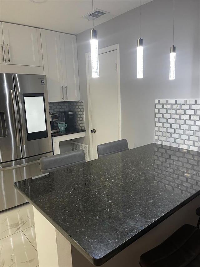 kitchen with stainless steel refrigerator, white cabinetry, dark stone countertops, and decorative backsplash