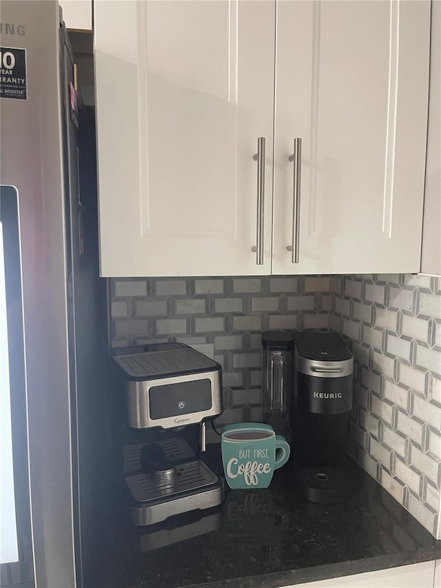 details featuring white cabinets, decorative backsplash, stainless steel fridge, and dark stone countertops