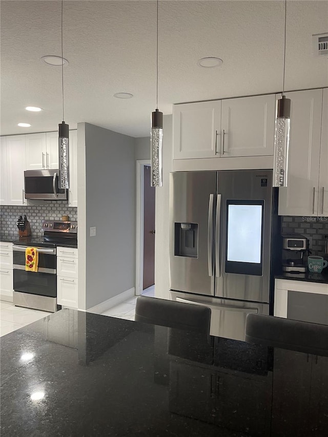 kitchen with backsplash, hanging light fixtures, dark stone countertops, white cabinetry, and stainless steel appliances