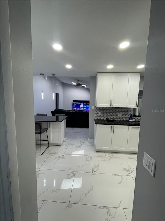 kitchen with pendant lighting, a breakfast bar, backsplash, white cabinets, and ceiling fan