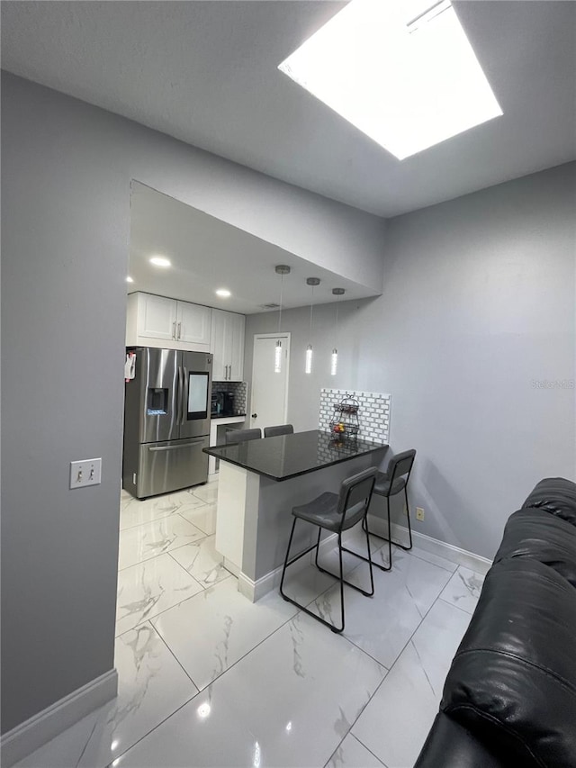 kitchen with hanging light fixtures, a kitchen breakfast bar, stainless steel refrigerator with ice dispenser, kitchen peninsula, and white cabinets