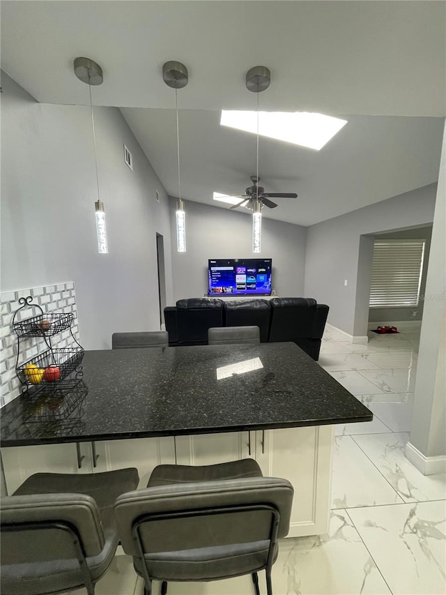 kitchen featuring ceiling fan, hanging light fixtures, dark stone counters, a breakfast bar, and white cabinets