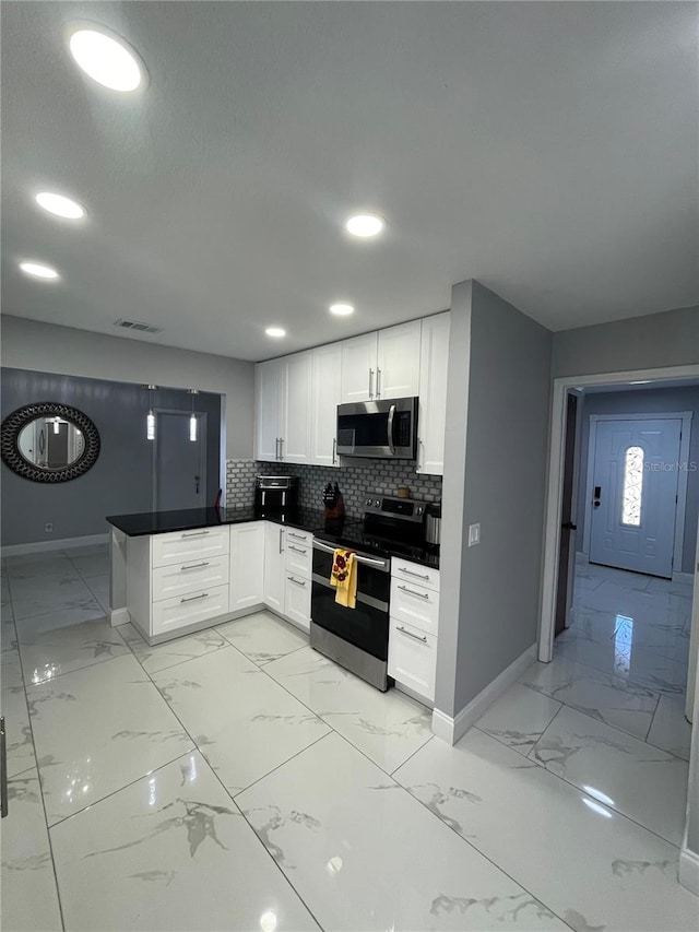 kitchen with kitchen peninsula, appliances with stainless steel finishes, tasteful backsplash, and white cabinetry