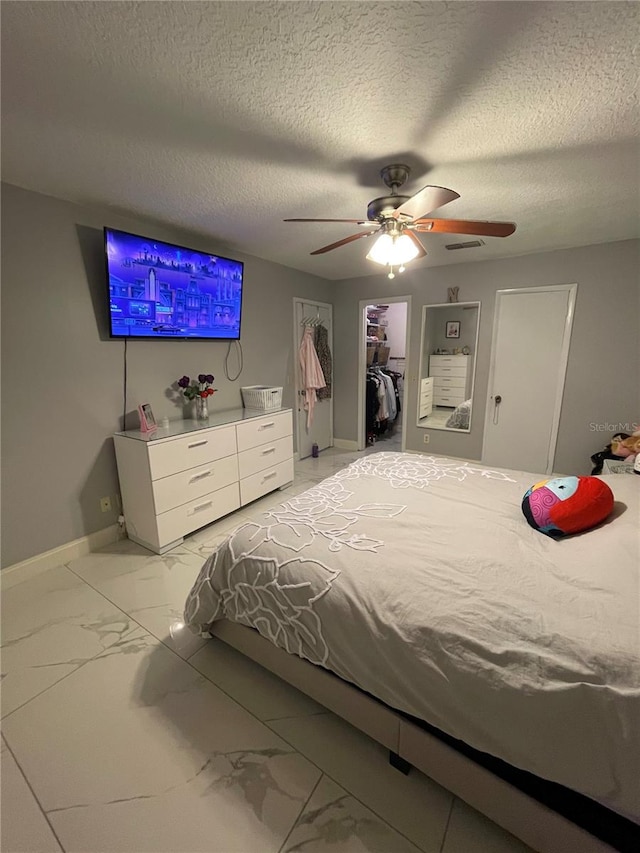 bedroom with a walk in closet, a textured ceiling, a closet, and ceiling fan