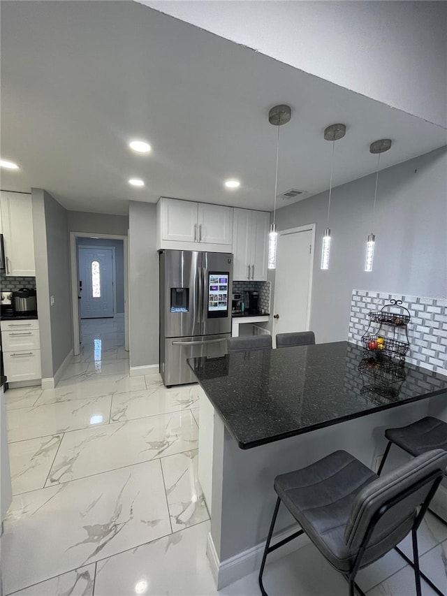 kitchen featuring white cabinets, stainless steel fridge with ice dispenser, pendant lighting, and dark stone countertops