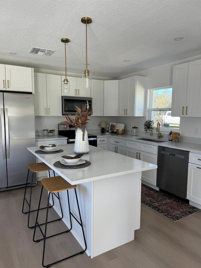 kitchen with white cabinetry, sink, a center island, hanging light fixtures, and appliances with stainless steel finishes