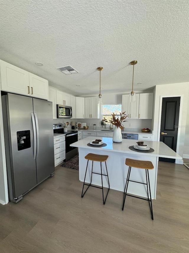 kitchen featuring pendant lighting, a center island, white cabinets, and stainless steel appliances