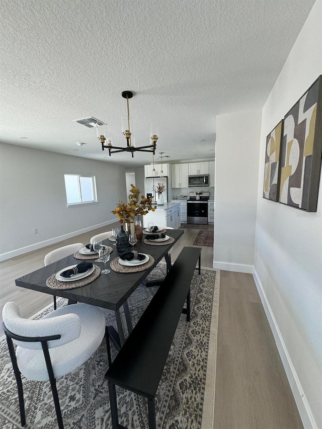 dining area with hardwood / wood-style floors, a textured ceiling, and an inviting chandelier