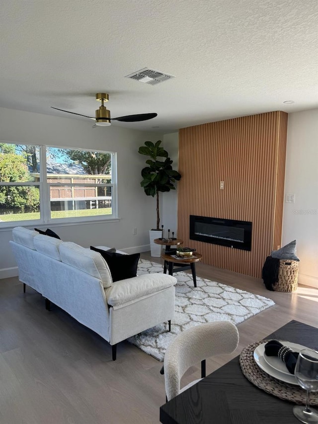 living room featuring hardwood / wood-style flooring, ceiling fan, and a textured ceiling