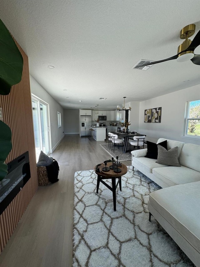 living room featuring ceiling fan with notable chandelier, a textured ceiling, and hardwood / wood-style flooring