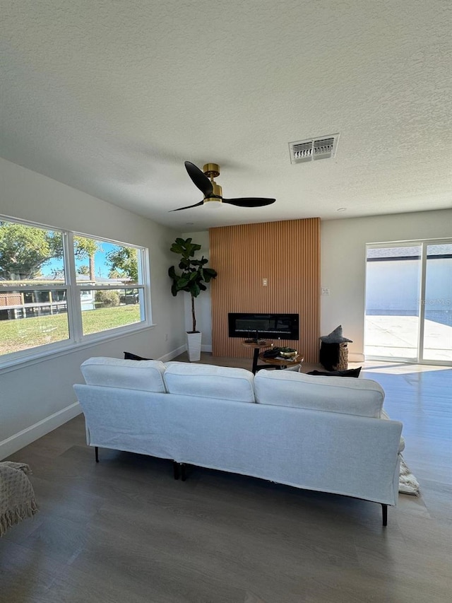 living room featuring ceiling fan, a fireplace, and a textured ceiling