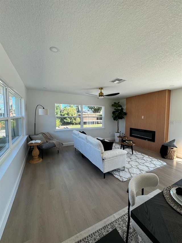 living room with ceiling fan, a large fireplace, wood-type flooring, and a textured ceiling