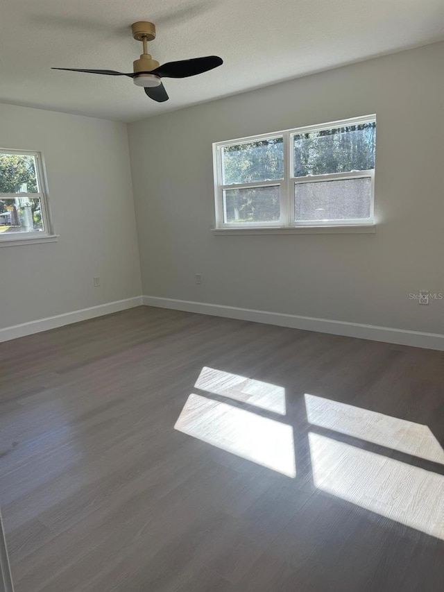 empty room with ceiling fan, a healthy amount of sunlight, and dark hardwood / wood-style flooring