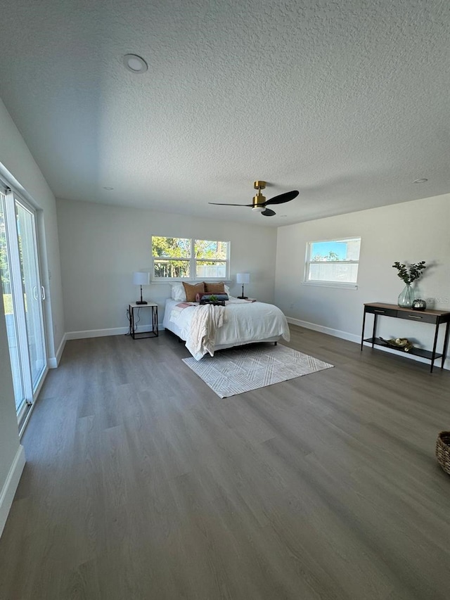 unfurnished bedroom featuring ceiling fan, access to exterior, wood-type flooring, and multiple windows