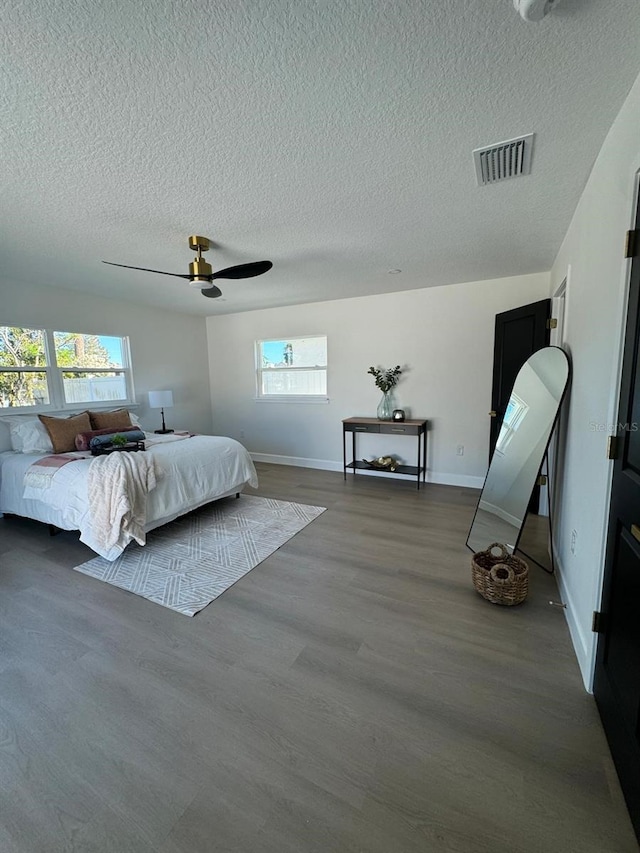 bedroom with hardwood / wood-style floors, a textured ceiling, multiple windows, and ceiling fan