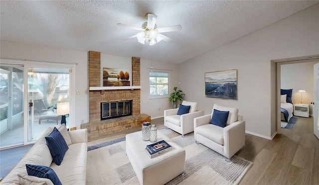 living room featuring lofted ceiling, ceiling fan, a fireplace, a textured ceiling, and light wood-type flooring